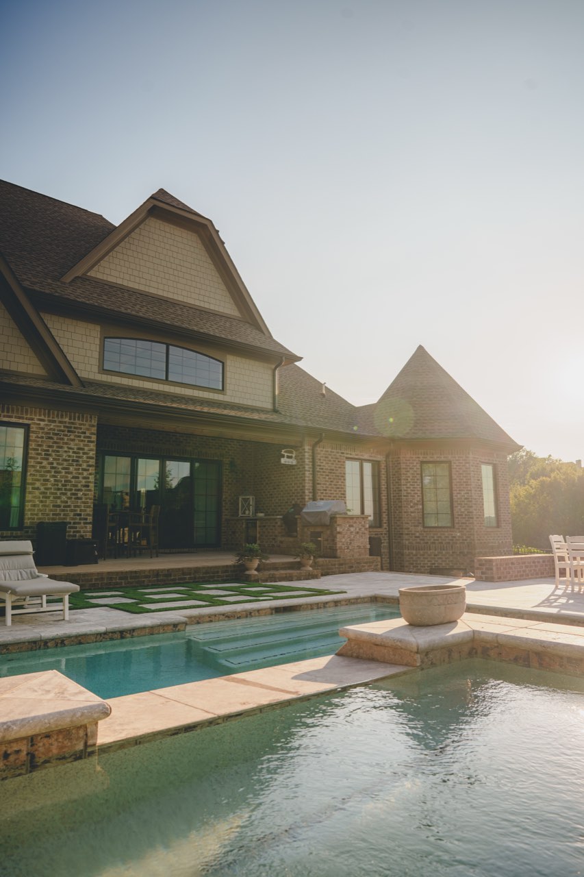Pool, Spillover Spa & Turf-Inlay Deck Behind a Brick Estate