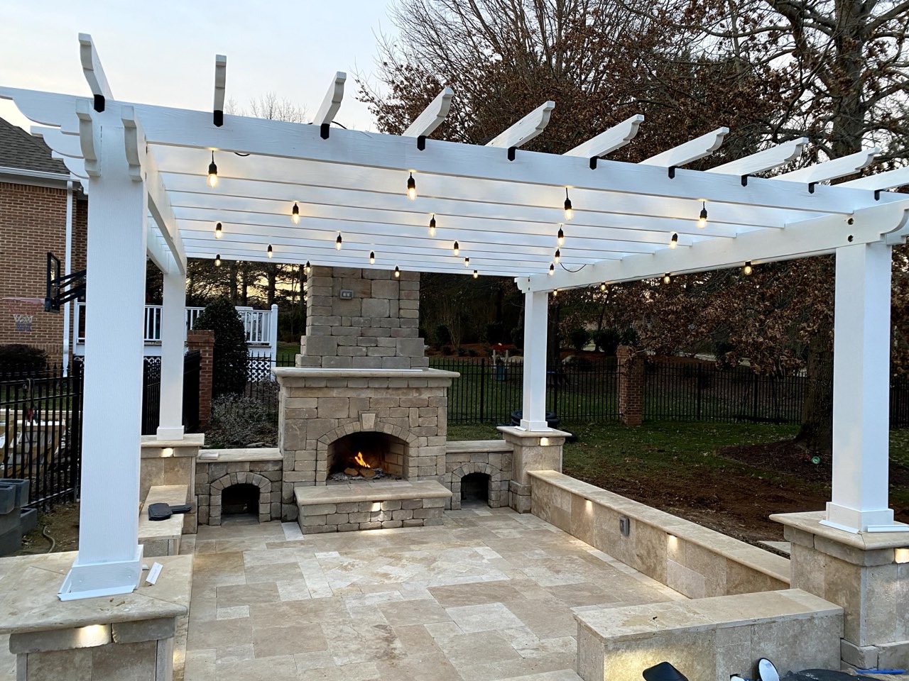 Pergola Patio With Stone Fireplace And String Lights At Dusk